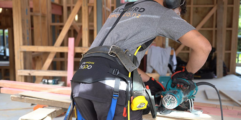 A person wearing the HAPO exoskeleton around their back and waist as they work at a construction site.